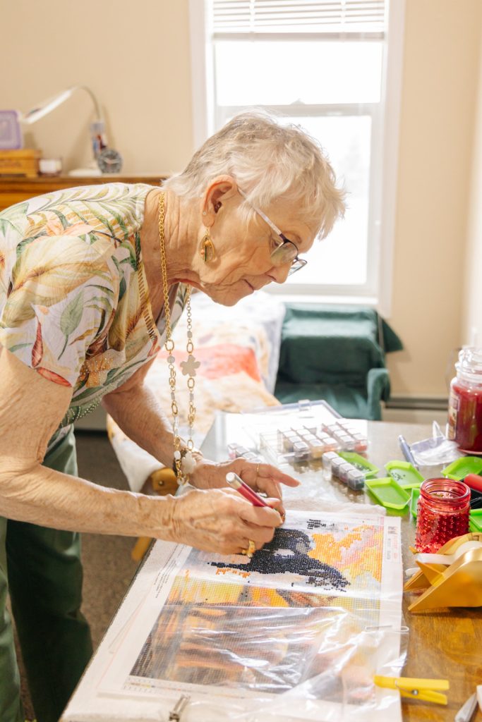Senior female resident focused on a diamond painting art project at her table at Harvest House assisted living, Olds Alberta