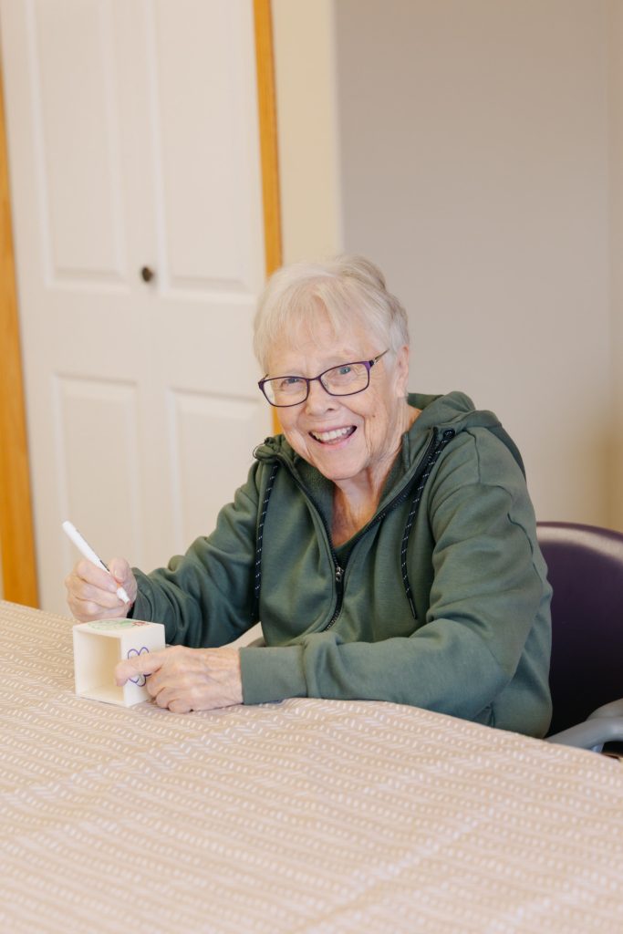 Senior female resident smiling warmly in the Harvest House common area in Olds, Alberta