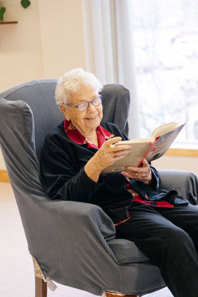 Senior woman enjoying reading in a cozy chair at Harvest House senior living in Olds