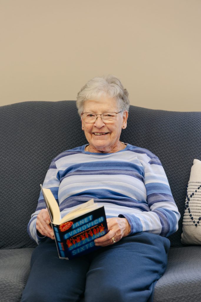 Senior female resident smiling on a sofa while enjoying a novel at Harvest House senior living in Olds, Alberta