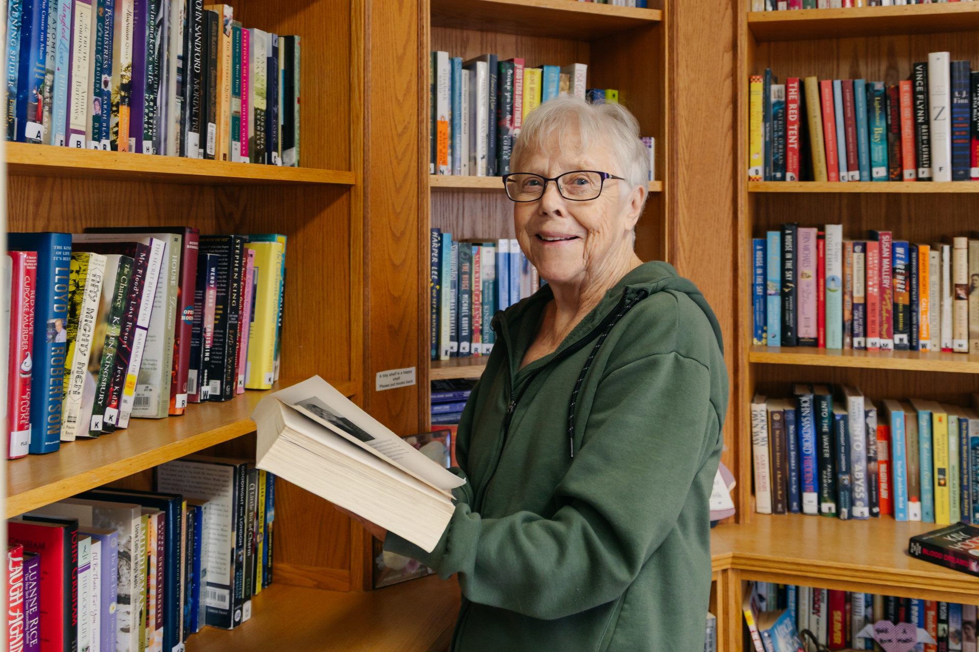 Senior female resident smiling while browsing books in the Harvest House community library in Olds, Alberta