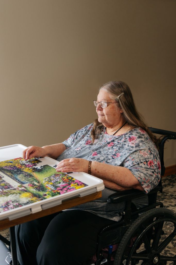 Senior female resident in a wheelchair independently enjoying a jigsaw puzzle on a lap tray at Harvest House assisted living, Olds Alberta