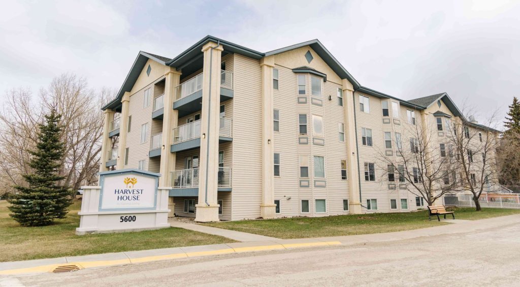 Exterior of Harvest House senior living at 5600 Sunrise Crescent in Olds, Alberta, showing the multi-storey building and entrance signage